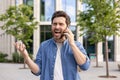 Angry and frustrated young man emotionally talking on mobile phone on city street near office center, shouting and Royalty Free Stock Photo