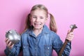 Angry funny young girl with silver piggy bank and hammer on pink background. save money concept. Royalty Free Stock Photo