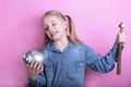 Angry funny young girl with silver piggy bank  and hammer on pink background. save money concept. Royalty Free Stock Photo