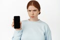 Angry ginger girl showing empty phone screen. Woman with mobile phone furrows while shows her smartphone interface, bad Royalty Free Stock Photo