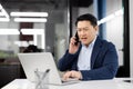 Angry grumpy boss shouting while talking on the phone, experienced asian man in business suit with phone in hands Royalty Free Stock Photo