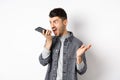 Angry guy shouting at speakerphone, scream on mobile phone, leaving angry voice message, standing against white Royalty Free Stock Photo