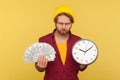 Angry hipster bearded guy in checkered shirt holding big clock and dollars banknotes, looking at camera