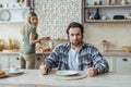 Angry hungry dissatisfied millennial caucasian man with stubble ignoring woman and wait for food in kitchen