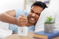 Angry indian man with alarm clock lying in bed