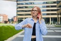 Angry irritated young business woman holding mobile phone and looks at his watch at the blurry business center building Royalty Free Stock Photo