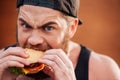 Angry irritated young man eating hamburger outdoors Royalty Free Stock Photo