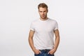 Angry, judgemental handsome macho blond male model in white t-shirt, look offended or angry, squinting aggressive