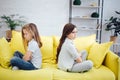 Angry and mad girls sit on yellow sofa in room. They dont` look at each other. Girls are very upset.