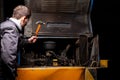 An angry male mechanic is repairing the engine of an old truck with an open hood hitting it with a hammer Royalty Free Stock Photo