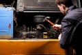 An angry male mechanic is repairing the engine of an old truck with an open hood hitting it with a hammer Royalty Free Stock Photo