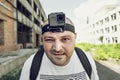 Angry man with action camera on head looking at camera and go. Portrait of travel blogger in urban background