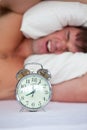 Angry man in bed annoyed by his alarm clock