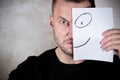 Angry man covers half his face with a piece of paper with a painted smile Royalty Free Stock Photo