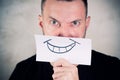 Angry man covers his mouth with a sheet with a painted smile Royalty Free Stock Photo