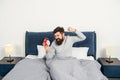 Angry man figting with alarm clock being in bed in morning, overslept