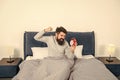 Angry man figting with alarm clock being in bed in morning, overslept
