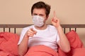 Angry man in medical mask pointing his finger at you sitting in the bed at home Royalty Free Stock Photo