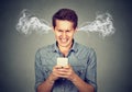 Angry man reading a text message on smartphone blowing steam coming out of ears