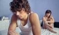 Angry man sitting over bed with woman on background Royalty Free Stock Photo