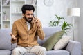 Angry angry man talking on the phone at home, dissatisfied customer sitting on the sofa in the living room yelling at Royalty Free Stock Photo