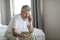 Angry middle aged man sitting on bed, have phone conversation Royalty Free Stock Photo