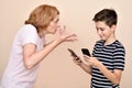 Angry mother scolding her smiling son with two smartphones