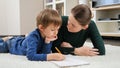 Angry mother scolding and talking to her silly son doing homework on floor in living room. Concept of domestic education Royalty Free Stock Photo