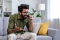 Angry and nervous man talking on the phone sitting on the sofa in the living room, hispanic man yelling at the Royalty Free Stock Photo