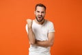 Angry nervous young man in casual white t-shirt posing isolated on bright orange background studio portrait. People