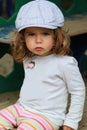 Angry one year old girl in a checked cap sitting offended on playground