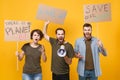 Angry protesting young three people hold protest signs broadsheet placard scream in megaphone isolated on yellow