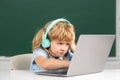 Angry sad child boy in headphones using a laptop and study online with video call teacher at school. Little funny system Royalty Free Stock Photo