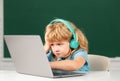 Angry sad child boy in headphones using a laptop and study online with video call teacher at school. Little funny system Royalty Free Stock Photo
