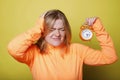 Angry sad woman holding her head with one hand and orange big clock in other over yellow background. Depression deadline concept