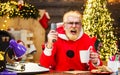 Angry Santa Claus sitting in armchair watching Christmas movie and drinks coffee. New Year cinema. Royalty Free Stock Photo