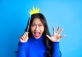 Angry screaming woman with paper crown on stick isolated on blue background.