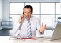 Angry senior businessman in stress working and talking on mobile phone at computer desk Royalty Free Stock Photo