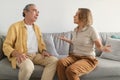 Angry senior spouses having quarrel, sitting on sofa and arguing, looking at each other and gesturing, side view Royalty Free Stock Photo