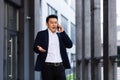 Angry and serious Successful Asian businessman explains information to employees using phone, speaks near office outside Royalty Free Stock Photo