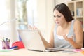 Angry student looking at laptop on a desk at home