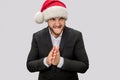 Angry and suspicious young man hold hands together. He looks to right. Guy wear Christmas hat and suit. Isolated on