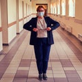 An angry teacher with a pointer in a medical mask stands in an empty school corridor. Woman teacher during isolation, coronavirus