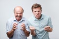 angry two men exclaim with negative emotions shout loudly, over white studio wall. Annoyed son and father have failure