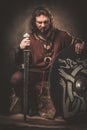 Angry viking with sword in a traditional warrior clothes, posing on a dark background.