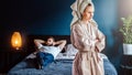 Angry woman in bathrobe stands in bedroom,her arms crossed over chest. Man is lying on bed .Couple having problems. Royalty Free Stock Photo