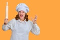 Angry woman chef with dough rolling pin in hand on studio background, copy space Royalty Free Stock Photo