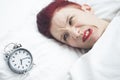 Angry woman lying in bed with alarm clock on pillow Royalty Free Stock Photo
