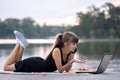 Angry woman talking angrily on mobile phone while working behind laptop computer lying down in summer park outdoors Royalty Free Stock Photo