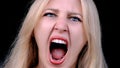 Angry woman yells in rage as she looking at camera on black background. Headshot of girl screaming into camera with her Royalty Free Stock Photo